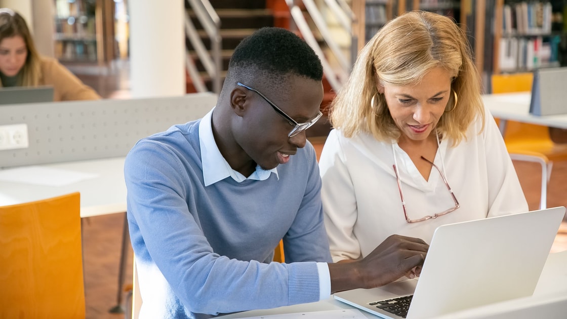 Duas pessoas revisam um notebook juntas durante uma sessão de aprendizado na biblioteca.