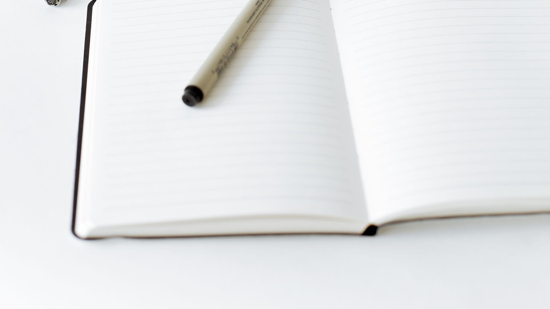 Caderno aberto com caneta e material de escrita sobre uma mesa clara.