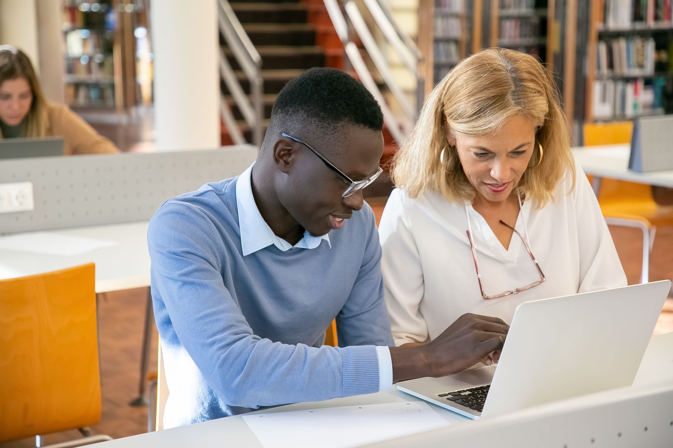 Uma professora e um aluno trabalham juntos em um notebook em uma biblioteca.