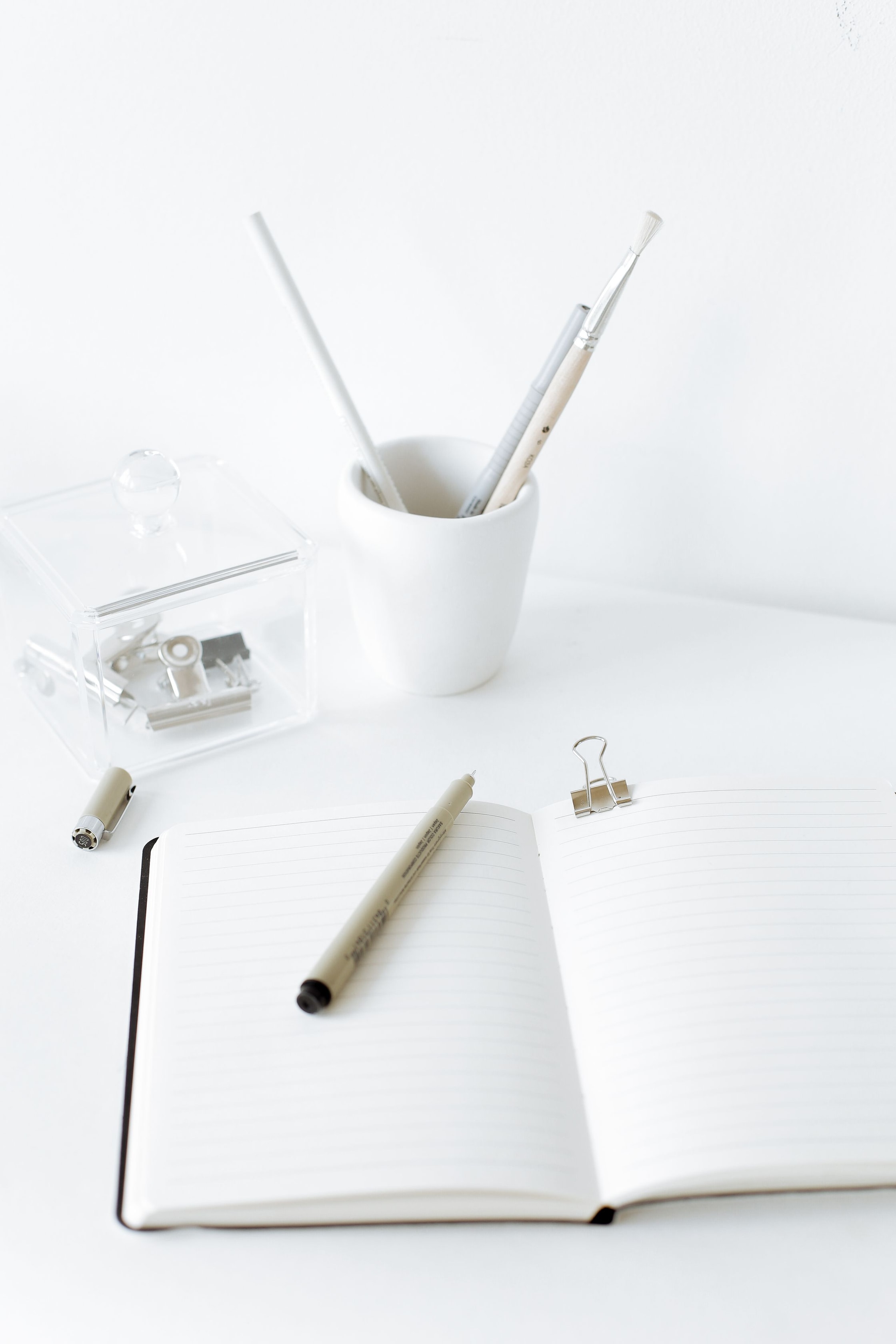 Caderno aberto com caneta e material de escrita sobre uma mesa clara.